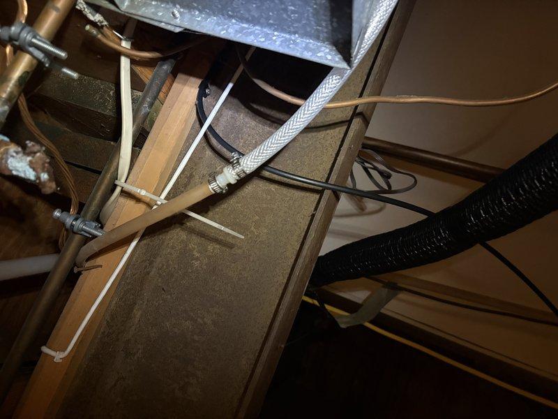 Responded to water leak complaint affecting basement area. Inspected exterior unit perimeter and foundation drainage system where water intrusion was occurring. Examined attic/ceiling space mechanical components including copper piping, ductwork, and condensate drainage lines. Documented conditions with photographs showing exterior landscaping area near unit and internal mechanical space with plumbing and HVAC systems. Identified source of water leak and completed necessary repairs to resolve basement water intrusion issue.