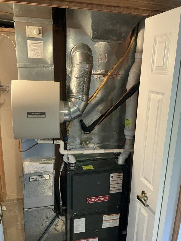 Responded to service call for non-operational air conditioning system at residential property. Upon arrival, conducted comprehensive evaluation of existing HVAC equipment including exterior Amana condenser unit with protective grille housing and interior Goodman furnace system with associated ductwork and Honeywell humidifier. Performed diagnostic assessment of both outdoor condensing unit and indoor air handler components to determine cause of system failure. Documented current equipment condition, configuration, and installation setup through photographic records showing condenser placement on mulched pad with electrical disconnect box, as well as mechanical room layout featuring furnace, plenum assembly, galvanized ductwork, and PVC drainage piping. Prepared detailed estimate for necessary repairs or equipment replacement options to restore cooling functionality to the residence.