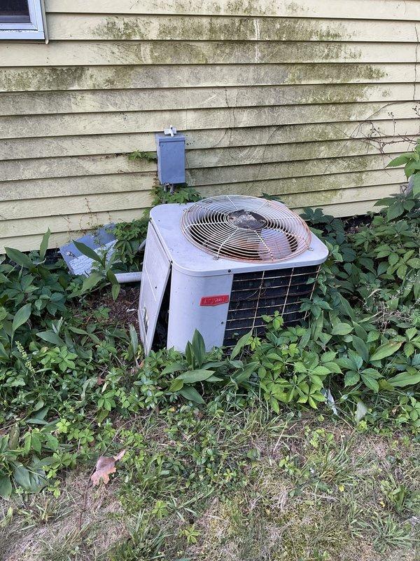 Responded to service call for air conditioning system not cooling properly with mild cooling still present. Upon inspection, identified refrigerant leak at outdoor condensing unit. Evaluated both outdoor condensing unit and indoor air handler system, documented equipment condition with overgrown vegetation surrounding outdoor unit requiring clearance for proper airflow and maintenance access. Provided estimate for refrigerant leak repair and system restoration.