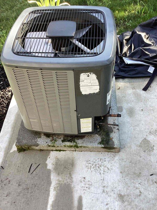 # Condenser Removal - Customer Waiting on Warranty

Documented existing outdoor air conditioning condenser unit for scheduled removal under warranty claim. Unit showed significant aging and environmental wear with faded cabinet finish, surface discoloration, and weathered components. Photographed condenser positioned on concrete pad with visible moss growth and staining. Documented refrigerant line connections and electrical service installation including weatherproof disconnect box mounted on metal conduit stand near basement window well. Return visit scheduled to complete condenser removal per warranty authorization.