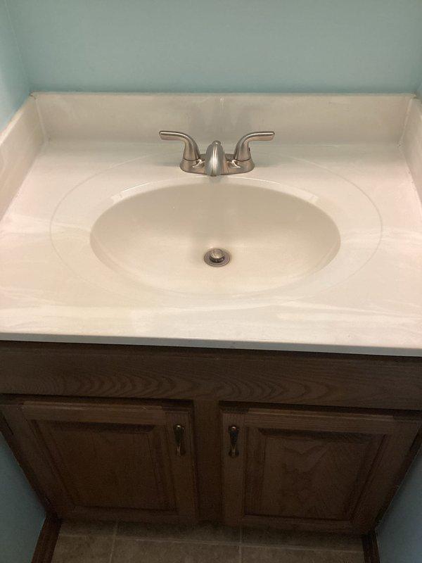 Responded to complaint of sewer odor emanating from shower drain for approximately two weeks in 1987-built home. Inspected shower floor drain and found significant accumulation of hair and organic debris on drain cover and within trap, which was causing odor issues and potentially compromising the trap seal. Removed debris buildup from drain assembly. Also inspected bathroom vanity sink per client request regarding slow drainage. Examined drain stopper mechanism and tested drainage flow. Documented conditions of both fixtures with photographs showing before-service state of shower drain with visible debris accumulation and bathroom vanity configuration with integrated sink basin and pop-up drain assembly.