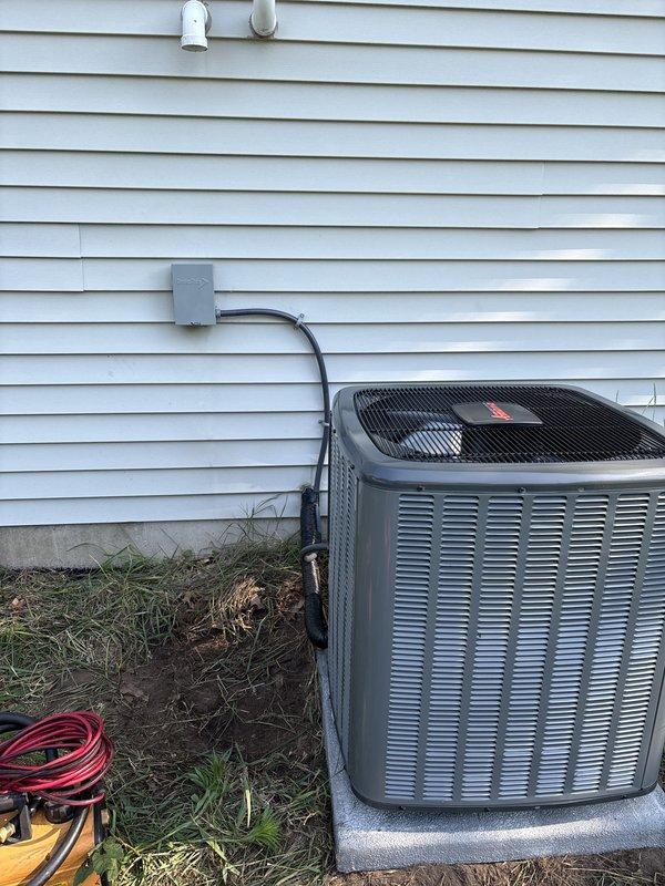 Complete air conditioning system replacement performed at residential property. Removed existing outdoor condenser unit and installed new AC condenser on concrete pad against exterior wall with light gray vinyl siding. Connected electrical service through gray disconnect box mounted on siding with conduit run to unit. Verified proper electrical connections, refrigerant charge, and system operation. Unit positioned on existing concrete foundation pad with adequate clearance for airflow and future service access. All electrical components secured and protected per code requirements. System tested and confirmed operational upon completion.