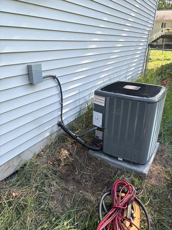Complete air conditioning system replacement performed at residential property. Removed existing outdoor condenser unit and installed new AC condenser on concrete pad against exterior wall with light gray vinyl siding. Connected electrical service through gray disconnect box mounted on siding with conduit run to unit. Verified proper electrical connections, refrigerant charge, and system operation. Unit positioned on existing concrete foundation pad with adequate clearance for airflow and future service access. All electrical components secured and protected per code requirements. System tested and confirmed operational upon completion.