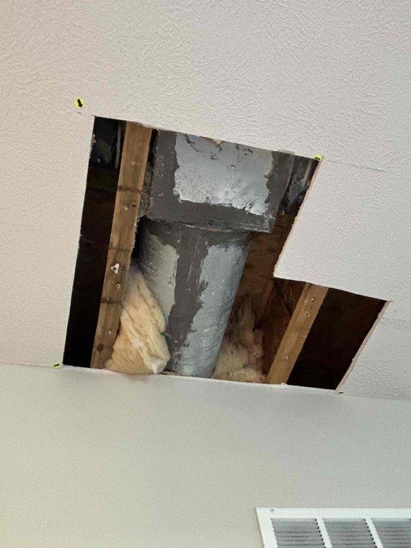 Responded to water leak in kitchen area caused by air conditioning condensing unit. Upon inspection, confirmed AC system was still operating and providing adequate cooling despite condensate drainage issue. Unit identified as seven-year-old LUXAIR system. Created multiple ceiling access points to inspect HVAC ductwork, insulation, and condensate drainage routing above affected area. Documented interior ceiling structure, exposed wooden joists, gray insulated ductwork components, and yellowish insulation material between structural elements. Access openings cut cleanly through drywall to evaluate extent of water intrusion and identify source of leak from condensing unit. Photographed all findings for documentation purposes.