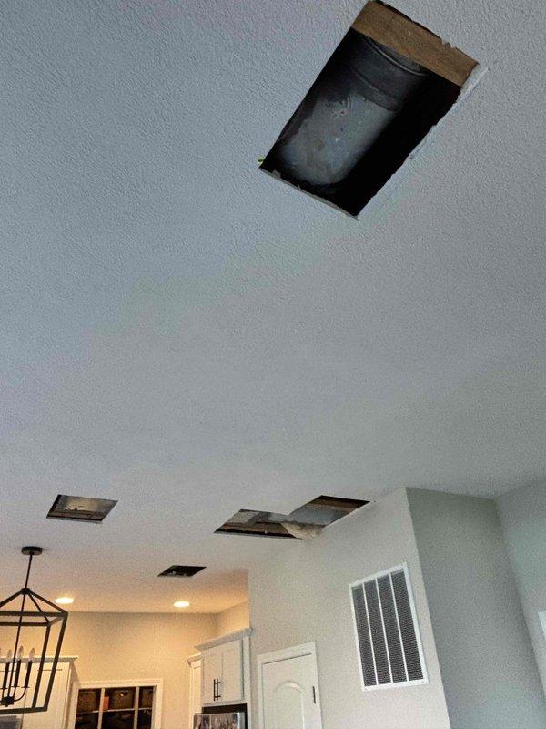 Responded to water leak in kitchen area caused by air conditioning condensing unit. Upon inspection, confirmed AC system was still operating and providing adequate cooling despite condensate drainage issue. Unit identified as seven-year-old LUXAIR system. Created multiple ceiling access points to inspect HVAC ductwork, insulation, and condensate drainage routing above affected area. Documented interior ceiling structure, exposed wooden joists, gray insulated ductwork components, and yellowish insulation material between structural elements. Access openings cut cleanly through drywall to evaluate extent of water intrusion and identify source of leak from condensing unit. Photographed all findings for documentation purposes.