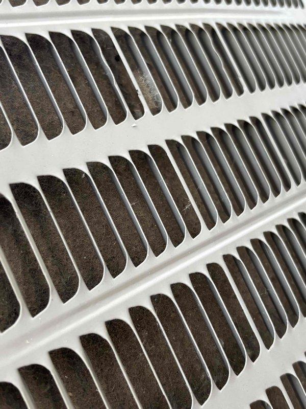 # Cooling System Service - 12-Year Goodman Unit

Responded to service call for inadequate cooling and weak airflow from furnace system. Upon arrival, customer reported unit was blowing warm air and failing to reach desired temperature setpoint.

Conducted visual inspection of air handling unit and evaporator coil assembly. Examination revealed significant accumulation of dirt and debris in condensate drain pan and surrounding areas, indicating extended period without maintenance. Return air grille showed restricted airflow pattern consistent with filtration or airflow obstruction issues.

Inspected evaporator coil housing and found evidence of dust buildup affecting heat transfer efficiency. Copper refrigerant lines displayed normal age-related patina consistent with 12-year-old equipment. Condensate drainage system showed dark residue accumulation that could potentially restrict proper drainage and affect system performance.

Documented equipment condition through photographic evidenc