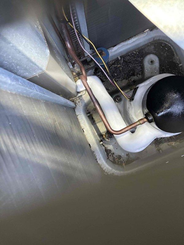 # Cooling System Service - 12-Year Goodman Unit

Responded to service call for inadequate cooling and weak airflow from furnace system. Upon arrival, customer reported unit was blowing warm air and failing to reach desired temperature setpoint.

Conducted visual inspection of air handling unit and evaporator coil assembly. Examination revealed significant accumulation of dirt and debris in condensate drain pan and surrounding areas, indicating extended period without maintenance. Return air grille showed restricted airflow pattern consistent with filtration or airflow obstruction issues.

Inspected evaporator coil housing and found evidence of dust buildup affecting heat transfer efficiency. Copper refrigerant lines displayed normal age-related patina consistent with 12-year-old equipment. Condensate drainage system showed dark residue accumulation that could potentially restrict proper drainage and affect system performance.

Documented equipment condition through photographic evidenc