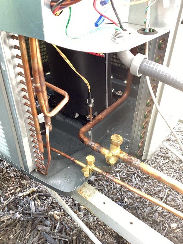 Returned to unit to diagnose previously quoted repair. Upon inspection, found significant corrosion and oxidation on copper refrigerant lines connected to the outdoor condensing unit. Observed moisture accumulation in the drain pan area and visible water residue on equipment surfaces, indicating potential condensate drainage issues. Documented condition of copper piping showing advanced tarnishing and discoloration, brass service valves, and finned coil assembly. Inspected electrical connections, wiring, and junction box components within the unit compartment. Photographed corroded copper lines, service valve connections, and overall system condition for repair documentation and customer records.