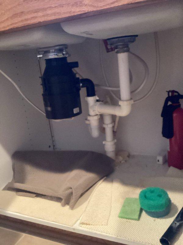 Responded to kitchen drain complaint with clogged left sink basin, non-functional garbage disposal, and foul odor. Accessed under-sink plumbing to diagnose disposal malfunction and drain blockage. Inspected P-trap configuration and disposal connections, cleared obstruction from drain line, and restored proper drainage flow to kitchen sink. Also addressed slow-draining bathtub during service visit.
