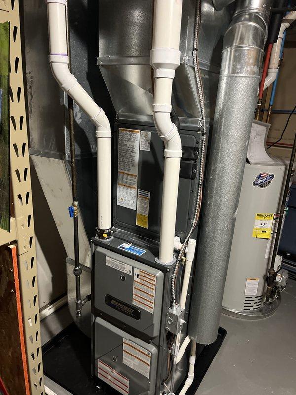 Completed full installation of residential HVAC system including furnace unit and air conditioning condenser. Installed dark gray furnace in mechanical room with proper venting using white PVC piping routed through utility space. Mounted outdoor AC condenser unit on concrete pad in landscaped area with appropriate refrigerant line connections and drainage piping along exterior wall. All equipment installed per manufacturer specifications with proper electrical connections, ductwork integration, and code-compliant venting. System tested and verified operational.