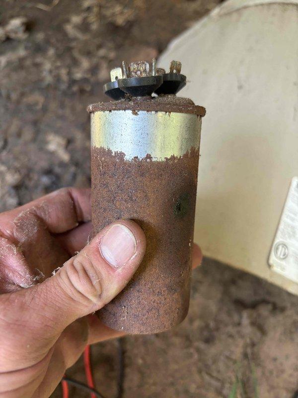 Responded to no-cooling complaint on 15-year-old air conditioning system. Upon inspection, found failed capacitor exhibiting severe corrosion and rust throughout the metal casing, indicating prolonged exposure to moisture and environmental elements. The capacitor's deteriorated condition prevented the compressor from starting, resulting in complete loss of cooling capability. Removed and replaced the failed capacitor with new component. Verified proper electrical connections and tested system operation. Unit restored to normal cooling function with compressor cycling properly and all electrical components operating within specifications.
