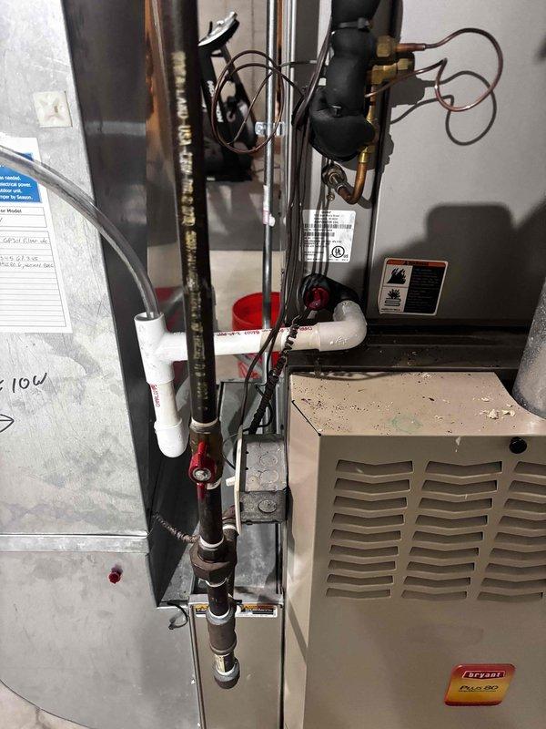 Responded to water leak near HVAC system and cooling failure. Upon inspection, identified active leak at condensate drain connection point with visible rust staining and moisture accumulation in drain pan beneath furnace and air handler unit. Documented system condition showing deteriorated PVC drain line connection and debris buildup affecting proper drainage. Assessed AC cooling issue in conjunction with moisture problem, photographed warning labels, piping configuration, and overall equipment condition for service records.