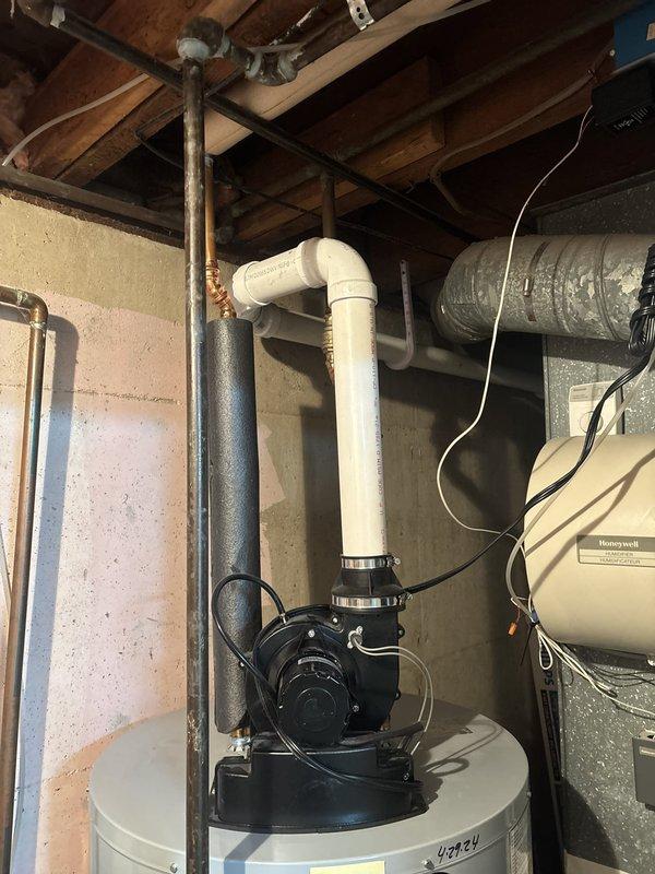 Responded to service call for water heater issues at residential property. Upon arrival, inspected LG brand water heater unit (model #40424) installed in basement utility area. Conducted thorough visual assessment of tank, plumbing connections, and associated components including top-mounted condensate pump with black motor assembly. Verified proper installation of white PVC venting system with elbow configuration extending from tank top. Examined all pipe connections, shut-off valves, and safety relief mechanisms for signs of leakage or malfunction. Inspected drain pan placement at base of unit and checked control box/sensor mounting. Documented current condition of water heater installation with photographs showing tank positioning, plumbing configuration, electrical connections, and surrounding mechanical systems. Confirmed proper clearances around unit and assessed overall installation compliance with manufacturer specifications. Unit operational at time of inspection.
