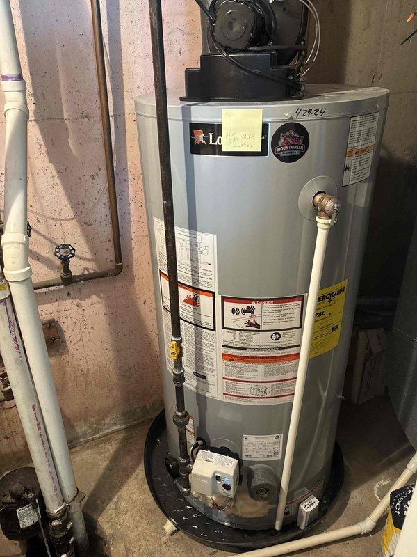 Responded to service call for water heater issues at residential property. Upon arrival, inspected LG brand water heater unit (model #40424) installed in basement utility area. Conducted thorough visual assessment of tank, plumbing connections, and associated components including top-mounted condensate pump with black motor assembly. Verified proper installation of white PVC venting system with elbow configuration extending from tank top. Examined all pipe connections, shut-off valves, and safety relief mechanisms for signs of leakage or malfunction. Inspected drain pan placement at base of unit and checked control box/sensor mounting. Documented current condition of water heater installation with photographs showing tank positioning, plumbing configuration, electrical connections, and surrounding mechanical systems. Confirmed proper clearances around unit and assessed overall installation compliance with manufacturer specifications. Unit operational at time of inspection.