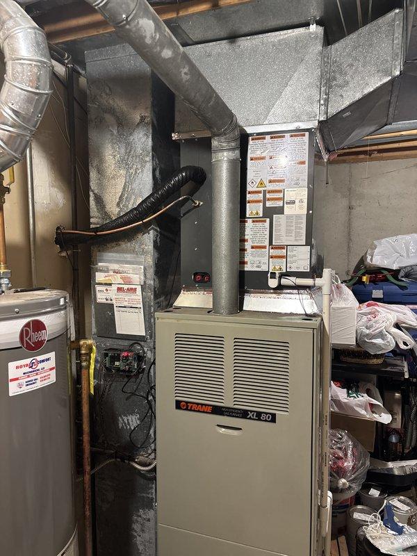 Completed full air conditioning system replacement including outdoor condenser unit and indoor furnace integration. Installed new tan-colored condenser unit on concrete pad with proper refrigerant line connections and electrical disconnect box mounted to exterior wall. Configured Trane XL 80 furnace in basement mechanical room to interface with new AC system, ensuring proper ductwork connections and airflow distribution throughout residence. All refrigerant lines properly insulated and secured to exterior siding with appropriate mounting brackets. System tested and verified operational, with financing paperwork processed and completed.