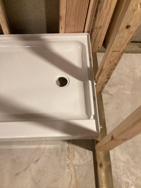 Completed finish plumbing installation in active construction area, setting and securing bathroom fixtures within newly framed structure. Successfully installed white fiberglass shower base with centered drain assembly on concrete slab, positioning unit within wooden stud framework for proper water containment and drainage. All fixtures were properly leveled, secured, and prepared for subsequent wall covering and trim work.