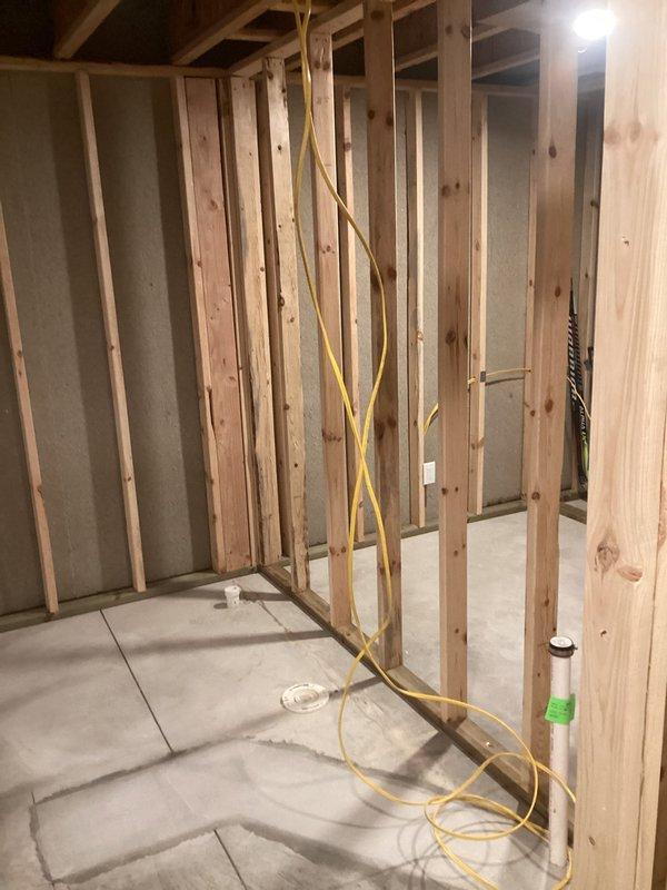 Completed finish plumbing installation in active construction area, setting and securing bathroom fixtures within newly framed structure. Successfully installed white fiberglass shower base with centered drain assembly on concrete slab, positioning unit within wooden stud framework for proper water containment and drainage. All fixtures were properly leveled, secured, and prepared for subsequent wall covering and trim work.