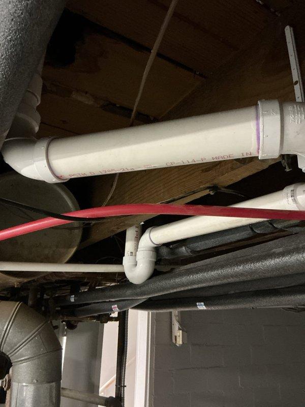 Completed basement drain repipe project involving replacement of existing drainage infrastructure with new PVC piping system. Installed large-diameter white PVC drain line with proper slope and fittings, including elbow joints for directional changes, ensuring code-compliant drainage flow. Work performed in utility area with existing water treatment equipment and copper supply lines, completed within one-day timeframe with minimal disruption to household operations.