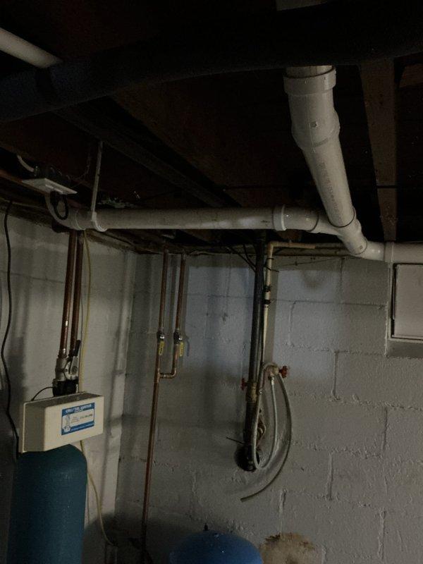 Completed basement drain repipe project involving replacement of existing drainage infrastructure with new PVC piping system. Installed large-diameter white PVC drain line with proper slope and fittings, including elbow joints for directional changes, ensuring code-compliant drainage flow. Work performed in utility area with existing water treatment equipment and copper supply lines, completed within one-day timeframe with minimal disruption to household operations.