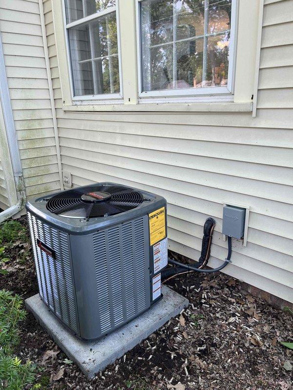 Completed full air conditioning system replacement at residential property. Removed existing outdoor condensing unit and installed new AC condenser on concrete pad with proper leveling and positioning. Established electrical connections via disconnect box with appropriate conduit routing along exterior siding. Verified refrigerant line connections between outdoor unit and indoor air handler located in basement mechanical room. Connected to existing furnace system with white PVC condensate drainage piping. Tested system startup, confirmed proper airflow through ductwork, verified electrical connections at disconnect, and ensured all safety labels and specifications were visible and intact. System operational and cooling effectively upon completion.