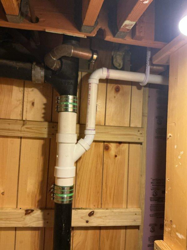Replaced kitchen drain line assembly beneath sink, including P-trap configuration and vertical drain pipe that showed evidence of water damage and deterioration at floor penetration. Installed new white PVC drainage system with proper trap configuration, chrome tailpiece connection to sink drain, and extended drainage piping through floor structure to connect with existing waste lines in basement/crawlspace below. All connections sealed and tested for proper drainage flow.