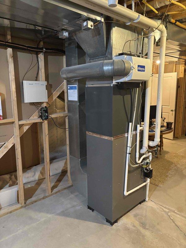 Complete air conditioning system replacement performed at residential property. Removed existing AC condenser unit and installed new outdoor condensing unit on concrete pad against exterior wall with proper clearances. Unit positioned on level concrete base with electrical disconnect box mounted to wall and refrigerant lines properly routed. Interior furnace system integration completed in basement mechanical room, including connection of ductwork, PVC condensate drainage, and electrical controls. All refrigerant lines charged to manufacturer specifications, system tested for proper operation, and airflow verified throughout distribution system.