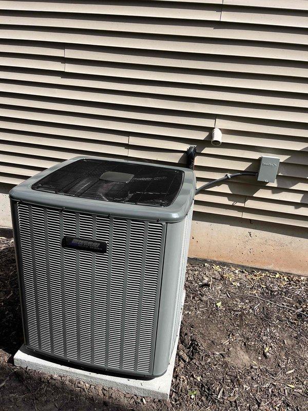 Complete air conditioning system replacement performed at residential property. Removed existing AC condenser unit and installed new outdoor condensing unit on concrete pad against exterior wall with proper clearances. Unit positioned on level concrete base with electrical disconnect box mounted to wall and refrigerant lines properly routed. Interior furnace system integration completed in basement mechanical room, including connection of ductwork, PVC condensate drainage, and electrical controls. All refrigerant lines charged to manufacturer specifications, system tested for proper operation, and airflow verified throughout distribution system.