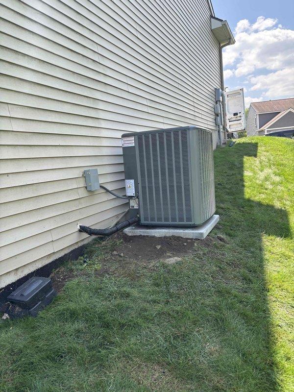 Completed full HVAC system replacement including outdoor condensing unit and indoor air handler with ENERGY STAR rated furnace. Removed existing equipment and installed new gray-green condensing unit on concrete pad with proper clearances from structure. Mounted electrical disconnect box on exterior siding and ran conduit from house to unit per code requirements. Inside installation included dark cabinet furnace with integrated humidifier system, white PVC exhaust and intake venting configured in dual-pipe arrangement, and condensate drain pan positioned beneath unit for proper water management. Verified all electrical connections, refrigerant line sets, and drainage systems operational. System tested and confirmed proper operation of heating and cooling cycles.