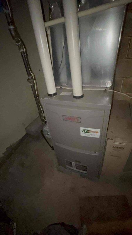 Responded to service call for HVAC system producing buzzing noise and causing electrical interference with household lights. Upon inspection, found 36-year-old Lennox unit with inadequate cooling performance and persistent buzzing that remained unresolved following recent electrical work. Documented existing furnace installation and ductwork configuration in basement utility area. Photographed equipment setup including flexible metallic ductwork, PVC venting system, and gas line connections to assess overall system condition and identify potential electrical or mechanical failure points causing the reported symptoms.