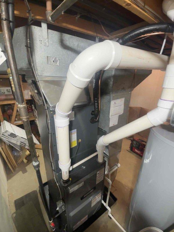 Completed full HVAC system replacement in residential basement mechanical room. Removed existing furnace and air conditioning equipment. Installed new gray air handler unit with proper base platform mounting on concrete floor. Connected silver metal supply ductwork with elbow joints to existing ceiling distribution system. Ran and secured copper refrigerant line set along wall from indoor unit. Installed white PVC condensate drain piping with proper pitch and trap configuration. Verified all electrical connections to furnace unit and confirmed proper voltage supply. Tested system startup sequence, airflow, and temperature differential. Confirmed all manufacturer labels and warning stickers properly displayed on equipment. System operational and performing to specifications upon completion.