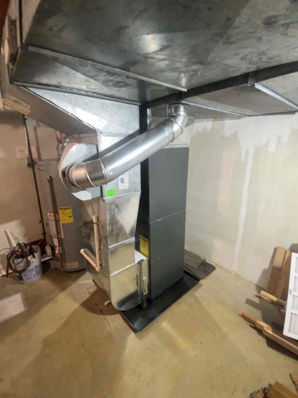 Completed full HVAC system replacement in residential basement mechanical room. Removed existing furnace and air conditioning equipment. Installed new gray air handler unit with proper base platform mounting on concrete floor. Connected silver metal supply ductwork with elbow joints to existing ceiling distribution system. Ran and secured copper refrigerant line set along wall from indoor unit. Installed white PVC condensate drain piping with proper pitch and trap configuration. Verified all electrical connections to furnace unit and confirmed proper voltage supply. Tested system startup sequence, airflow, and temperature differential. Confirmed all manufacturer labels and warning stickers properly displayed on equipment. System operational and performing to specifications upon completion.