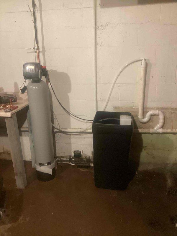Installed 30,000 grain capacity water softener system in basement utility area with complete plumbing connections. System includes primary softener tank with digital control head, brine tank, and associated copper and PVC supply lines properly connected to existing water infrastructure. Installation completed per manufacturer specifications with all components operational and ready for service.