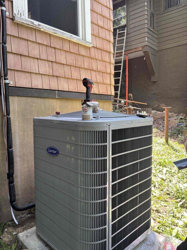 Completed installation of new Carrier brand air conditioning condensing unit in exterior side yard location. Unit was positioned on concrete pad against building exterior, with proper clearances maintained for optimal airflow and service access. All refrigerant lines, electrical connections, and drainage systems were installed and tested to manufacturer specifications, with system confirmed operational upon completion.