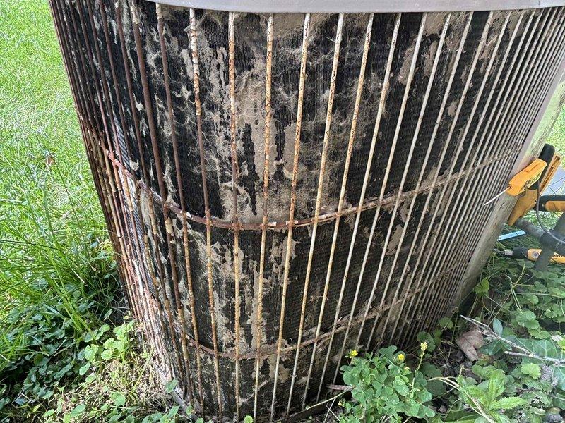 Responded to service call for air conditioning system not adequately cooling residence after extended period of non-use. Upon arrival, performed visual inspection of outdoor condenser unit and found extensive accumulation of dirt, debris, and organic matter coating the condenser coils and protective grille. The heavy buildup was significantly restricting airflow through the unit, reducing heat exchange efficiency and overall cooling capacity. Cleaned condenser coils and exterior surfaces to restore proper airflow and system performance. Verified electrical connections at disconnect box were secure and operational.
