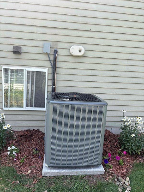 Completed full HVAC system installation including new furnace and air conditioning unit at residential property. Exterior condensing unit installed on concrete pad with proper electrical conduit routing and disconnect box mounted to exterior wall. Interior air handler and furnace positioned in basement utility area on raised platform with white PVC condensate drainage and exhaust venting installed per manufacturer specifications. All equipment properly mounted, leveled, and secured with refrigerant lines connected between outdoor and indoor units. System tested and verified operational.