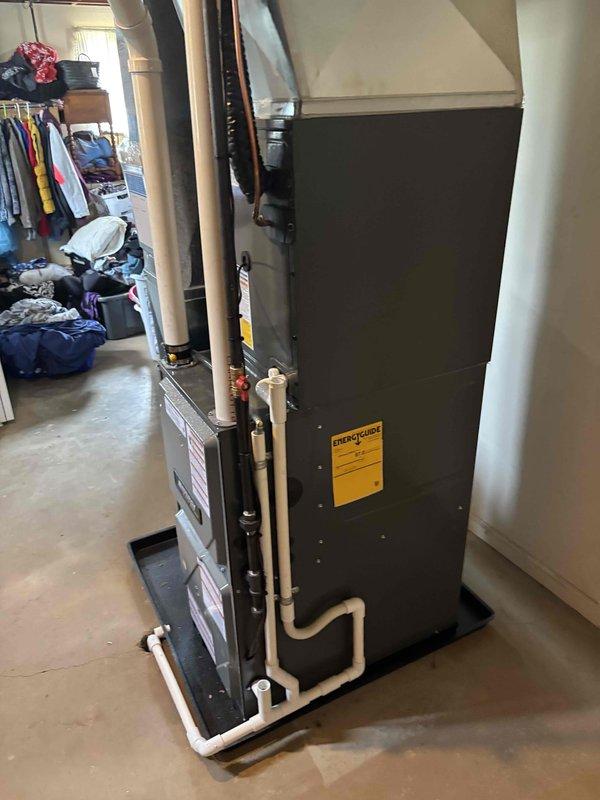 Completed full HVAC system installation including new furnace and air conditioning unit at residential property. Exterior condensing unit installed on concrete pad with proper electrical conduit routing and disconnect box mounted to exterior wall. Interior air handler and furnace positioned in basement utility area on raised platform with white PVC condensate drainage and exhaust venting installed per manufacturer specifications. All equipment properly mounted, leveled, and secured with refrigerant lines connected between outdoor and indoor units. System tested and verified operational.