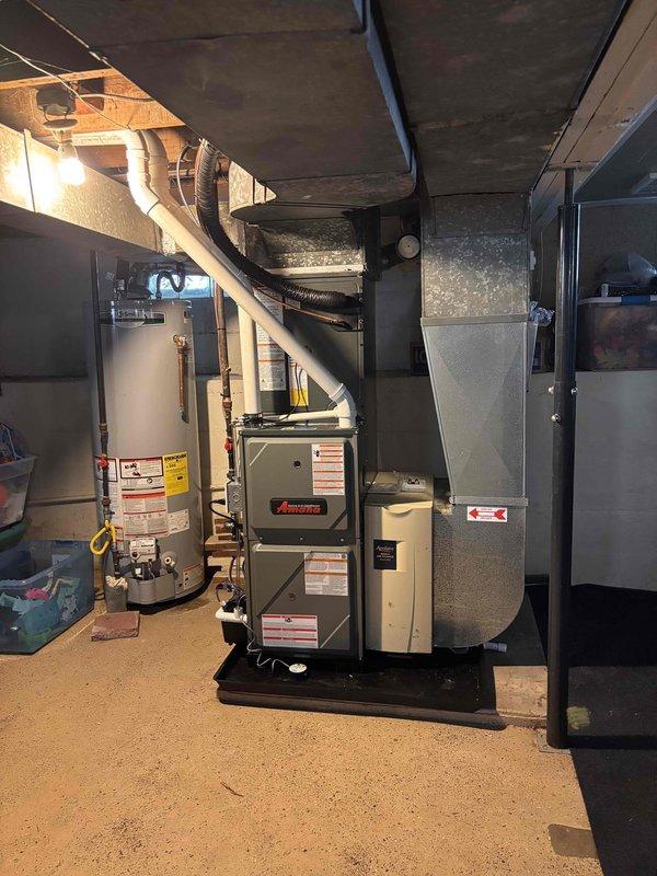 Completed full HVAC system installation including new Amana furnace and outdoor AC unit. Furnace installed in basement mechanical room on platform with proper ductwork connections to existing plenum system. Outdoor condensing unit positioned on concrete pad adjacent to structure with refrigerant lines and electrical connections completed. All equipment secured, tested, and operational per manufacturer specifications.