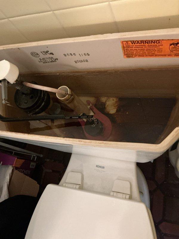 Responded to report of constant dripping leak in toilet ongoing for one week to one month in 1934-built home. Removed tank lid and inspected Kohler toilet tank components. Found deteriorated flapper valve causing continuous water leak from tank to bowl. Documented existing condition showing mineral deposits and discoloration throughout tank interior, worn red rubber flapper, and dated fill valve assembly. Photographed tank interior components including flush valve, overflow tube, and manufacturing date code indicating unit from 2001. Replaced failed flapper valve with new component to restore proper seal and eliminate constant water flow.
