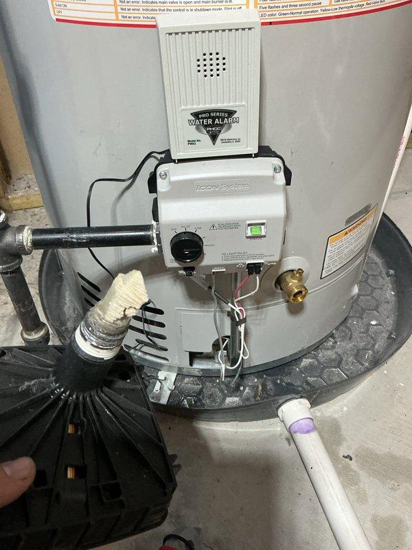 Completed water heater repair by replacing faulty gas valve assembly and burner components. Removed old gas valve with attached pilot assembly and flame arrestor screen, installed new replacement parts, and verified proper operation of Icon System control unit with green indicator light confirming successful ignition and temperature regulation.