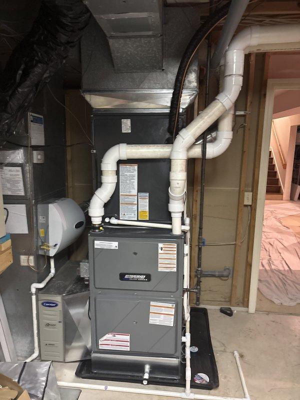 Completed full residential HVAC system replacement including installation of new Carrier outdoor condensing unit and indoor furnace assembly in basement utility area. Installed new white PVC condensate drainage piping, connected ductwork transitions, and mounted all equipment on appropriate platforms with proper electrical connections and refrigerant line sets. System tested and verified operational upon completion.