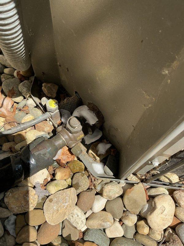 # No Cool Service Call

Responded to a complete system failure on a 2005 air conditioning unit. Upon arrival, found significant debris accumulation including leaves and organic material blocking the outdoor condenser unit's air intake and surrounding the refrigerant lines. Cleared all debris from the condenser base, protective screen, and around PVC piping to restore proper airflow. Inspected indoor mechanical components including copper refrigerant lines, valve assemblies, and condensate drainage system. Documented existing installation conditions with photographs showing utility space configuration with river rock ground cover and outdoor unit positioning against perimeter fencing. Verified all electrical connections and wiring routing at outdoor unit. System components showed age-appropriate wear consistent with nearly 20-year-old equipment. Removed obstructions that were preventing adequate heat exchange at condenser coil. Restored unit to operational status after clearing blockage