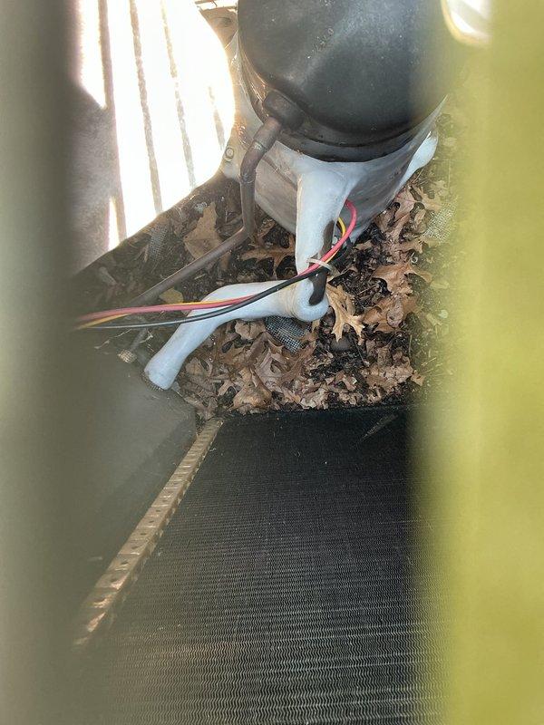 # No Cool Service Call

Responded to a complete system failure on a 2005 air conditioning unit. Upon arrival, found significant debris accumulation including leaves and organic material blocking the outdoor condenser unit's air intake and surrounding the refrigerant lines. Cleared all debris from the condenser base, protective screen, and around PVC piping to restore proper airflow. Inspected indoor mechanical components including copper refrigerant lines, valve assemblies, and condensate drainage system. Documented existing installation conditions with photographs showing utility space configuration with river rock ground cover and outdoor unit positioning against perimeter fencing. Verified all electrical connections and wiring routing at outdoor unit. System components showed age-appropriate wear consistent with nearly 20-year-old equipment. Removed obstructions that were preventing adequate heat exchange at condenser coil. Restored unit to operational status after clearing blockage