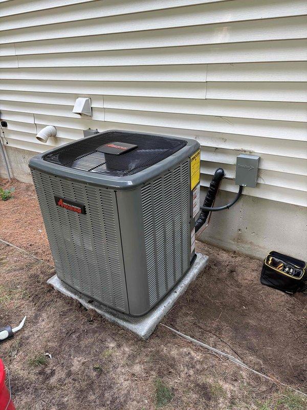 Successfully completed full air conditioning system replacement at residential property. Removed existing outdoor condensing unit and installed new Amana condenser on concrete pad adjacent to building exterior. Ran new refrigerant line set with proper insulation from outdoor unit to interior air handler, utilizing gray foam insulation on copper lines. Installed electrical disconnect box on exterior wall with appropriate conduit routing for power supply. Connected refrigerant lines with brass fittings and service valves, properly capped and secured all connections. Installed new PVC condensate drain line from unit through building siding. System was pressure tested, evacuated, and charged to manufacturer specifications. Verified all electrical connections, tested unit operation, and confirmed proper airflow through condenser fan assembly. Installation completed per manufacturer guidelines with all safety labels and warnings properly affixed to equipment.