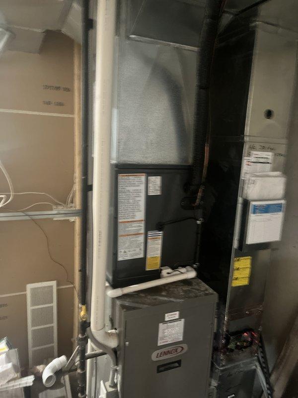 Completed full HVAC system replacement including outdoor condensing unit and indoor air handler components. Installed new gray outdoor AC unit on existing concrete pad against exterior wall with proper electrical disconnect and conduit routing through white vinyl siding. Mounted Lennox indoor equipment in mechanical closet below existing black furnace unit, ensuring proper integration with current heating system. Configured all necessary PVC condensate drainage lines and established proper clearances for service access. Verified all manufacturer labels and EnergyGuide documentation properly affixed to equipment. System tested and confirmed operational upon completion.