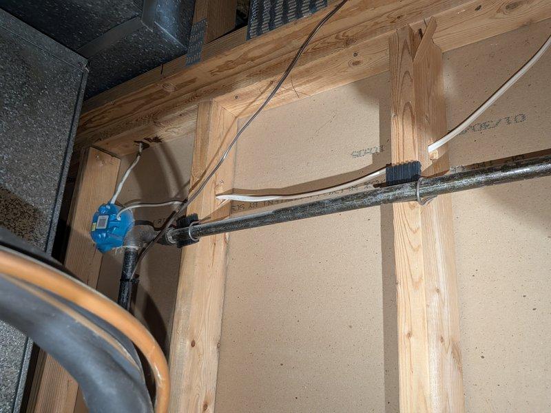 Responded to noise complaint regarding air conditioning system creating loud sounds through interior wall. Upon inspection, located source of noise in attic space where refrigerant lines and ductwork were improperly secured to wooden framing members. Found that vibration from compressor operation was being transmitted through inadequately fastened black insulated refrigerant line, causing resonance against wall studs and creating audible disturbance in living space. Properly secured all refrigerant lines with appropriate mounting brackets and added vibration-dampening isolation between pipes and framing to eliminate noise transfer. Verified system operation and confirmed noise issue resolved.