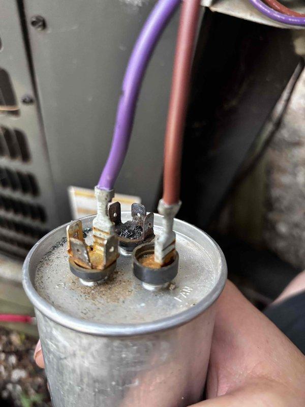 # Air Conditioner Not Cooling

Responded to no cooling complaint on residential air conditioning system. Upon inspection, discovered failed dual run capacitor with severely corroded terminals and evidence of electrical arcing. Terminal connections displayed heavy oxidation, burnt residue, and heat damage. One capacitor wire exhibited significant thermal damage with melted insulation and charring, indicating electrical failure under load.

Removed defective capacitor and damaged wiring. Installed new dual run capacitor with proper microfarad rating for compressor and condenser fan motor. Replaced burnt wire with appropriate gauge conductor and made secure connections to new capacitor terminals. Applied dielectric grease to terminal connections to prevent future corrosion. Verified all electrical connections were tight and properly insulated.

Energized system and confirmed compressor and outdoor fan motor operation. Measured supply voltage, amp draw on both circuits, and verified capaci