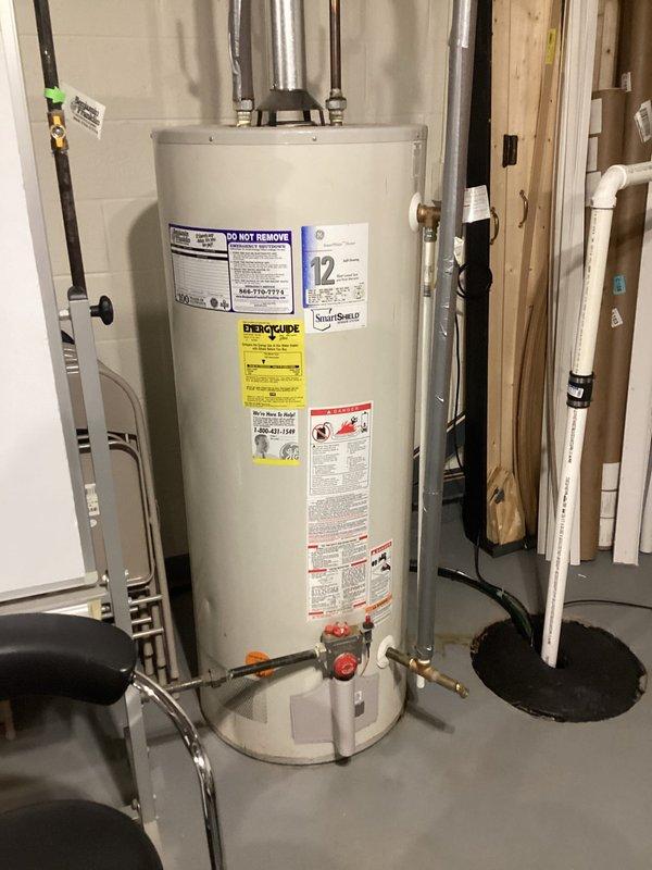 Provided estimate for replacement of existing 23-year-old 50-gallon conventional storage water heater with tankless water heating system for ranch-style residence. Evaluated current installation including venting configuration, gas supply line, and plumbing connections to determine requirements for tankless conversion capable of supporting whole-home demand with simultaneous operation of up to three shower fixtures. Documented existing equipment specifications and photographed current water heater installation showing top-mounted connections, flue pipe, and utility room layout to assess necessary modifications for tankless unit installation.