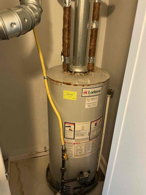 Completed water heater replacement estimate for residential property with 20-year-old Lochinvar unit showing significant corrosion on copper pipe connections and fittings at top of tank. Documented existing installation conditions including corroded hot and cold water connections, yellow flexible gas line, and metallic vent flue system, with recommendation for immediate replacement due to age and deterioration of plumbing connections.