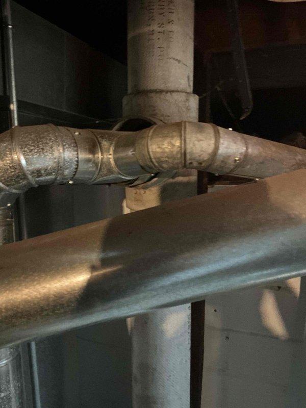 Responded to service call for 5-year-old water heater leaking from bottom. Upon inspection, identified active leak at base of unit near plumbing connections and valve assembly. Documented existing conditions including staining on concrete floor around heater base and configuration of inlet/outlet piping with red ball valves and copper fittings. Photographed water heater installation, mechanical room environment, and associated HVAC ductwork for service records.