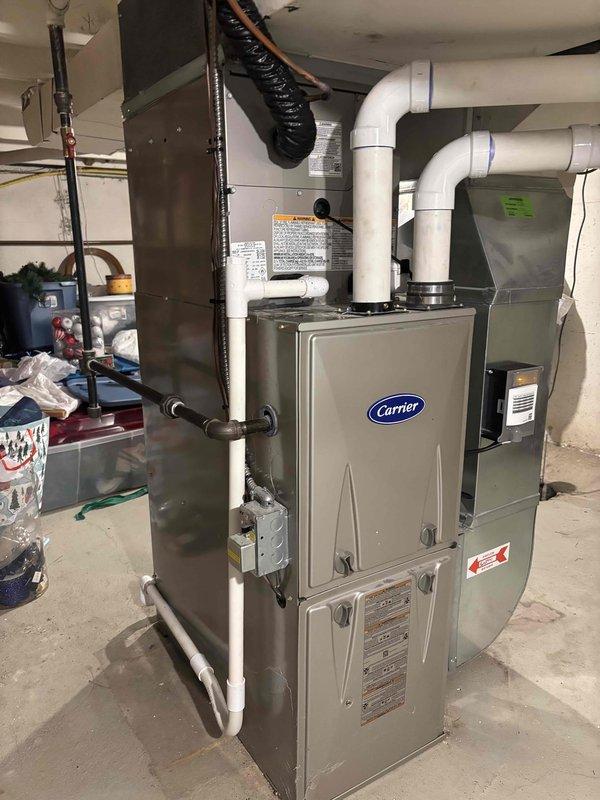 Completed full HVAC system replacement including outdoor condensing unit and indoor furnace. Installed new Carrier brand air conditioning condenser on existing concrete pad against exterior wall with proper clearances maintained. Unit positioned on stable foundation with adequate airflow access and protection from landscaping debris. Removed old equipment and set new outdoor unit with refrigerant line connections, electrical hookup, and condensate drainage properly configured.

Installed matching Carrier furnace in basement utility area with complete ductwork integration. Connected white PVC venting system with proper pitch and termination, installed gas line connections, and completed electrical wiring to code. Integrated system controls and verified all safety switches operational. Tested furnace ignition sequence, blower operation, and airflow distribution throughout duct system.

Charged refrigerant system to manufacturer specifications and verified proper subcooling and superheat 